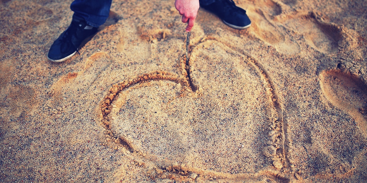person drawing a heart in the sand