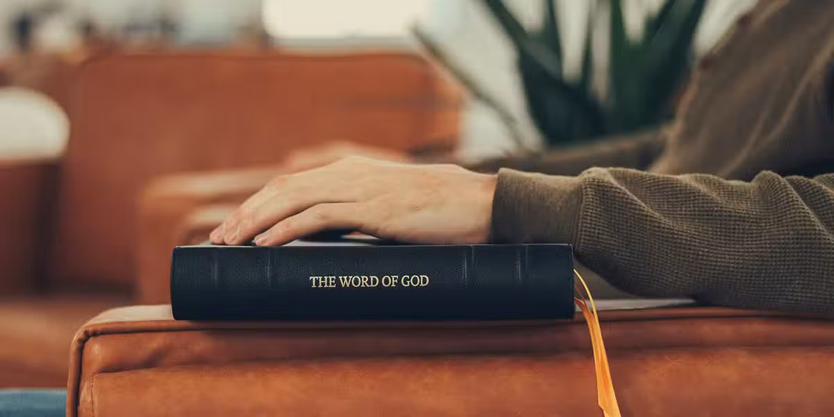 man resting hand on Bible while sitting in a chair
