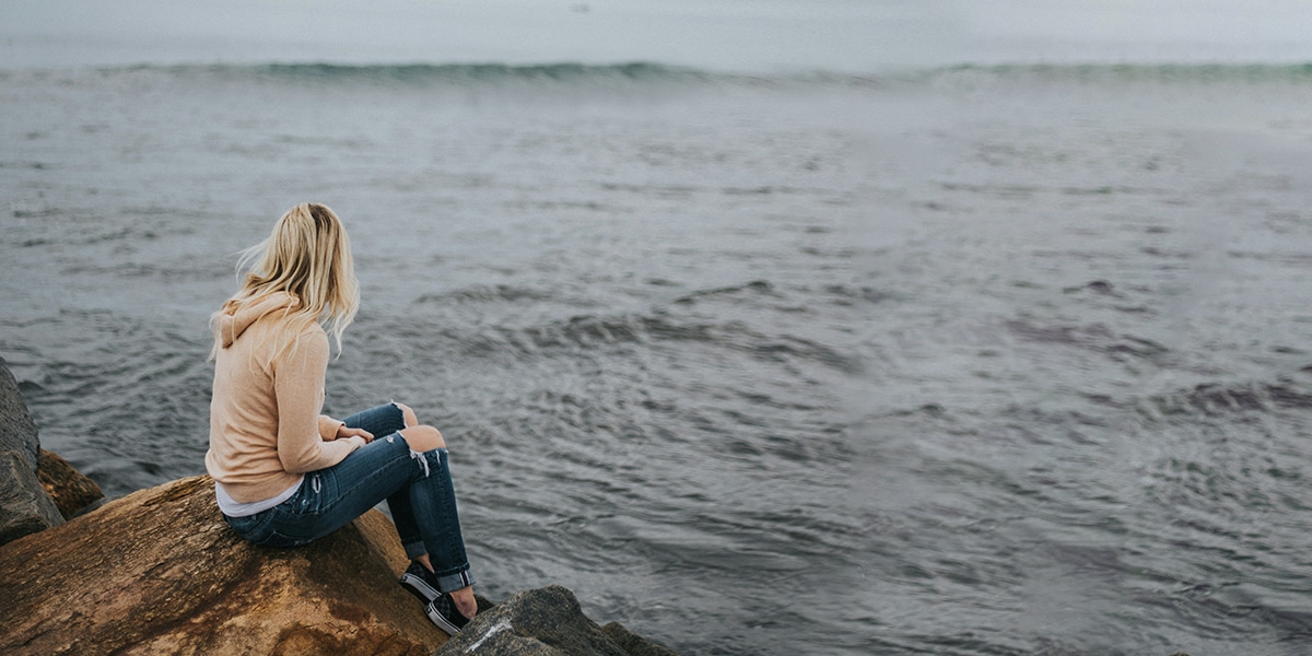 woman sitting on rocks by the ocean with waves in the distance.