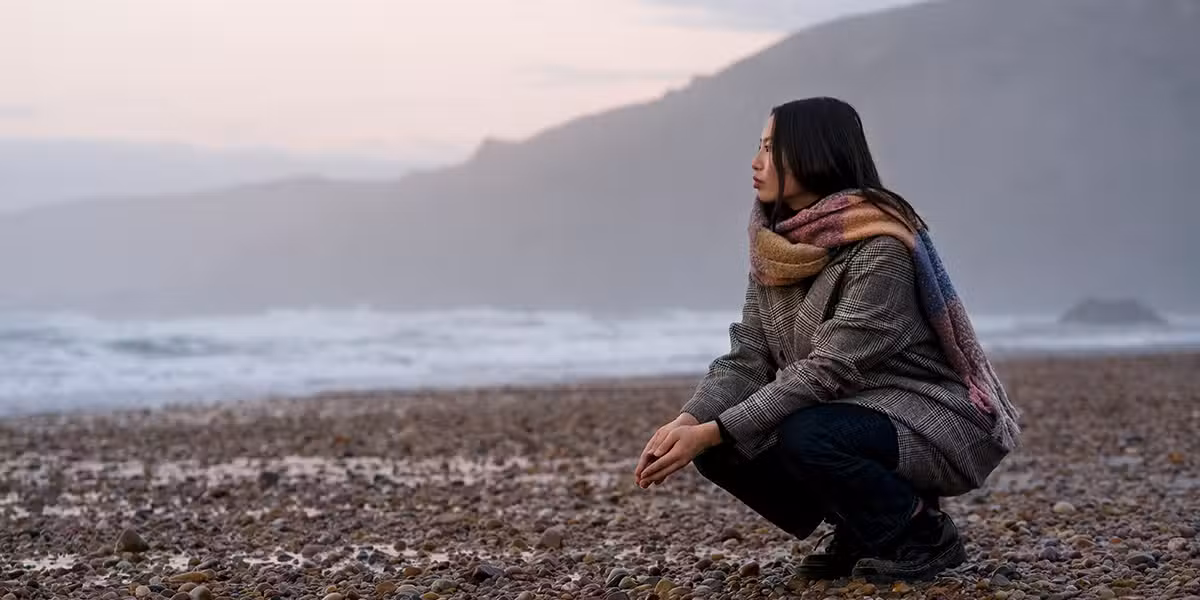 woman grieving and sad kneeling at a beach.